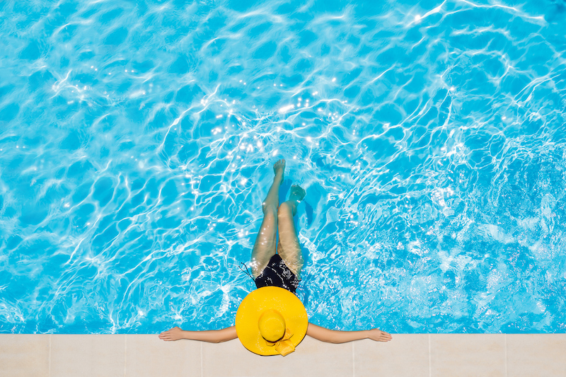 Woman sitting in a swimming pool in a large yellow sunhat