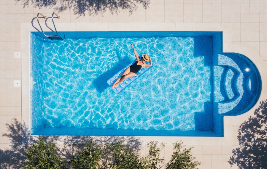 Young female in swimsuit bikini, in a straw hat and sunglasses floating on blue swimming pool waves on a float.