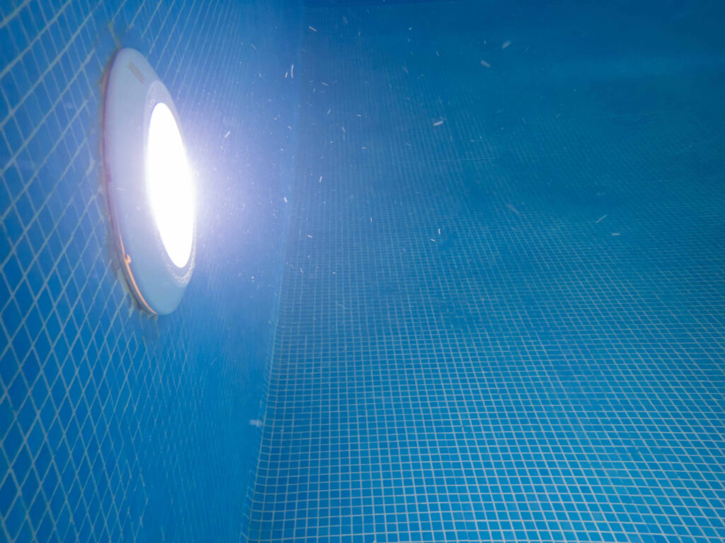 Underwater view of blue mosaic tile swimming pool interior with decorative tile, light, and water.