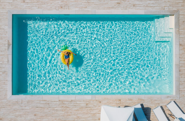 female in swimsuit bikini, in a straw hat and sunglasses floating on blue swimming pool waves on giant inflatable Yellow Pineapple tube. Chill out summer vacation in luxury resorts concept.