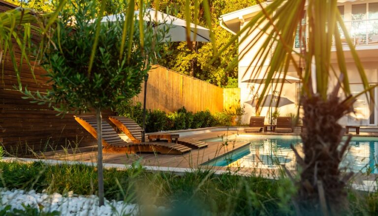 A serene poolside view at a tropical villa featuring lounge chairs surrounded by lush greenery and tropical plants