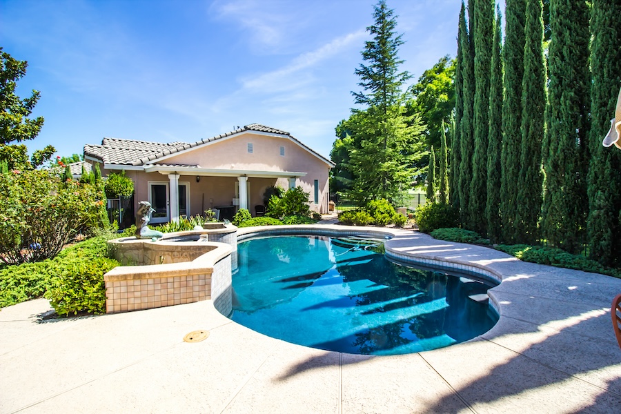 Free Form Swimming Pool With Fountain And Cypress Trees In Rear Yard Setting