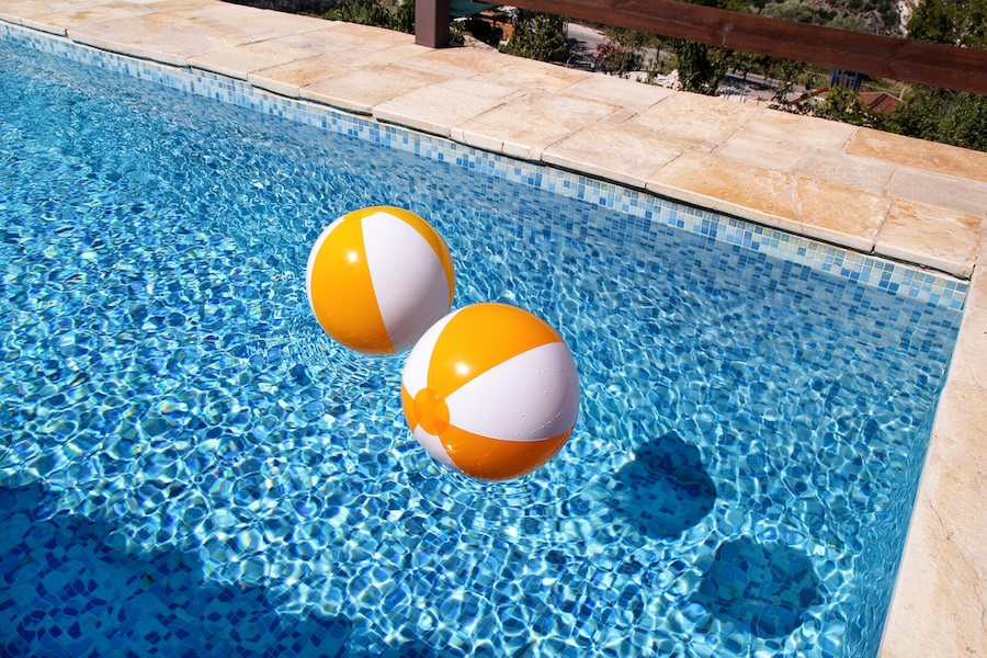 Two rubber air yellow white inflatable balls and toy for swimming pool in transparent blue water.