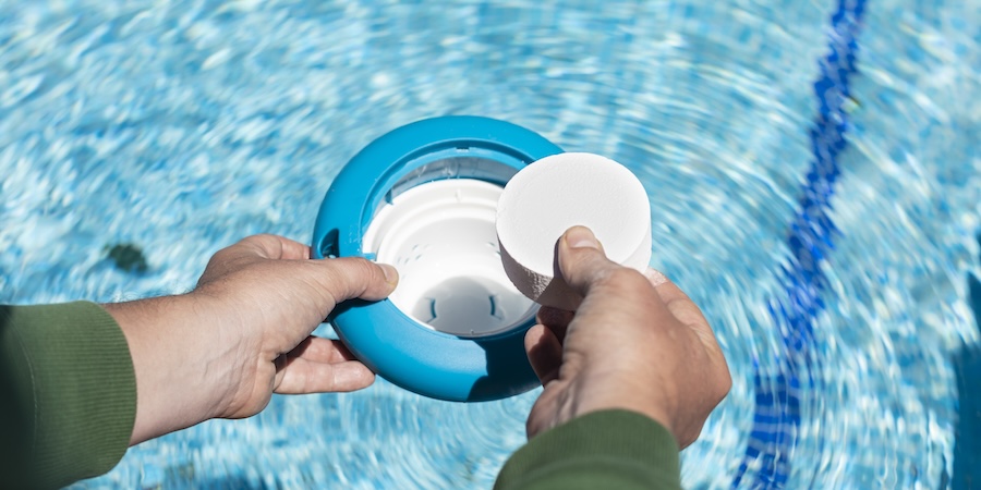 Hands adding chlorine tablets to pool