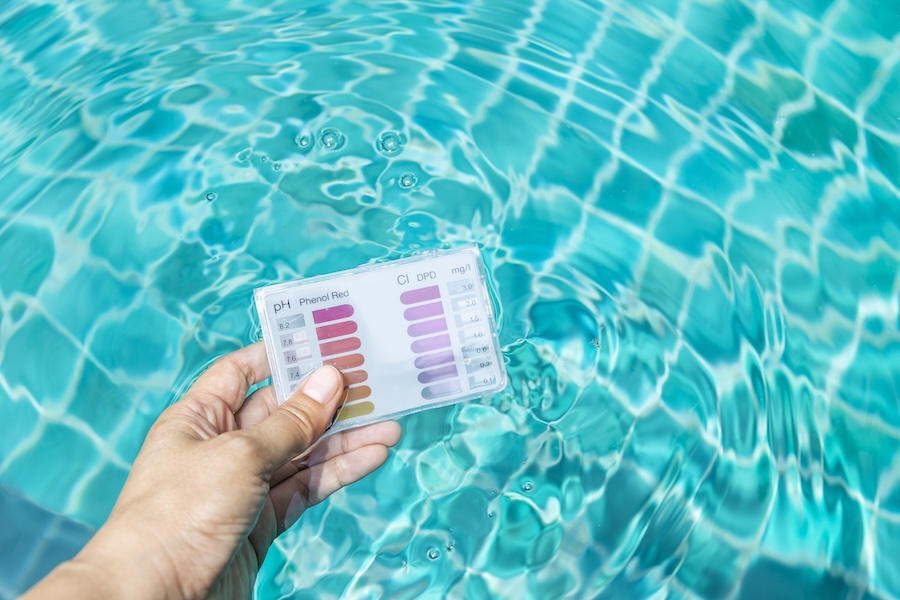 Swimming pool water testing test kit in girl hand dipping in clear water