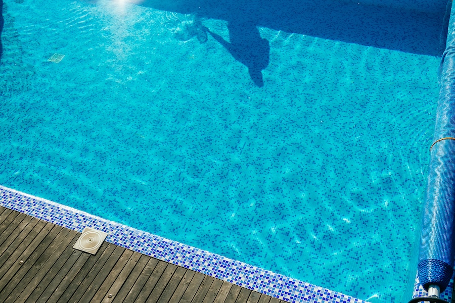 Man cleaning the swimming pool with vacuum equipment.
