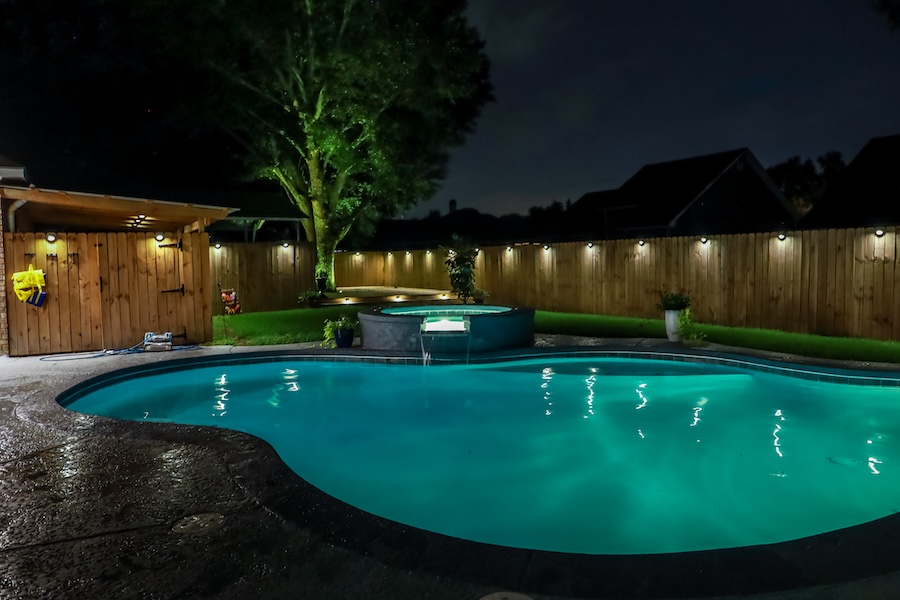 A backyard swimming pool and jacuzzi hot tob at night with solar lights