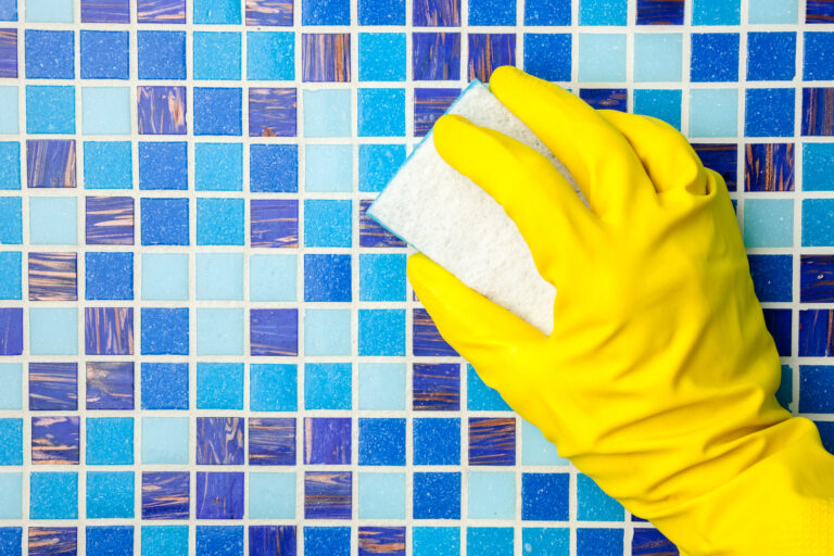 Hand in yellow protective glove cleaning mosaic pool wall