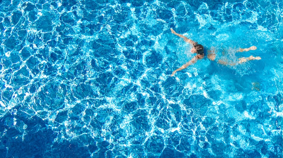 Aerial drone view of active girl in swimming pool from above