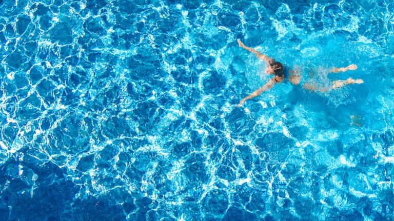 Aerial drone view of active girl in swimming pool from above