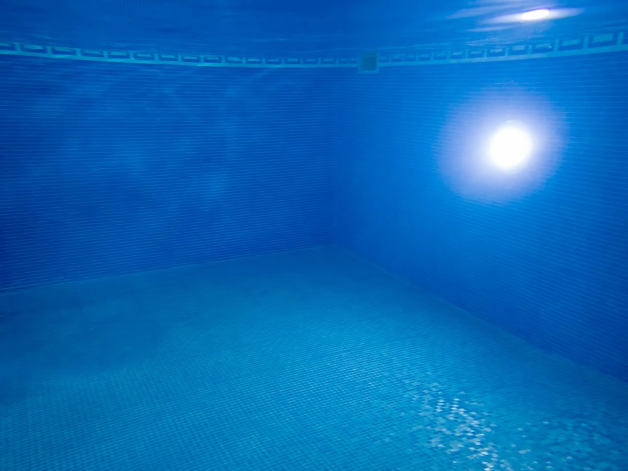 Underwater view of blue mosaic tile swimming pool interior with decorative tile and light
