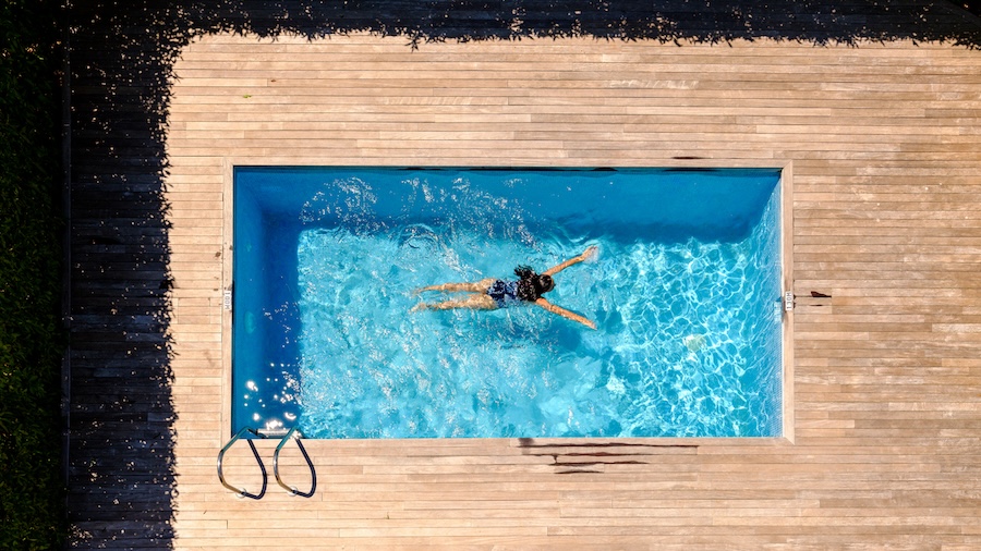 Drone view full length of unrecognizable woman with long wet dark hair floating in outdoor swimming pool