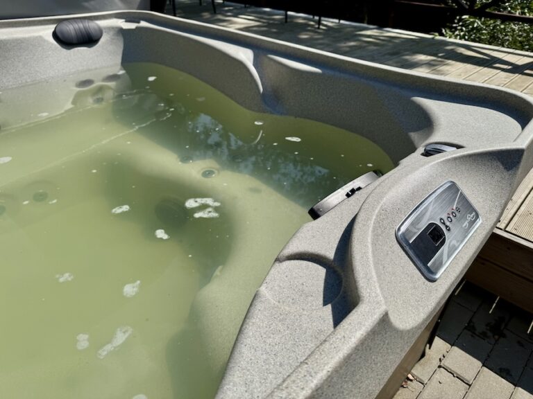 A neglected outdoor hot tub filled with murky green water covered in algae and contamination.