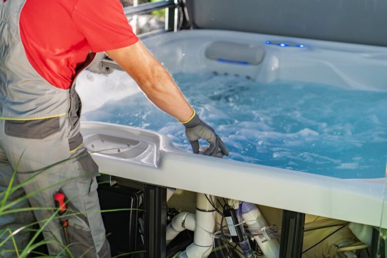 A SPA technician works carefully on a hot tub, ensuring its water is clean and functional while surrounded by lush greenery in a bright outdoor setting.
