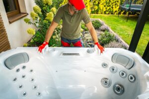 A professional in red gloves inspects and prepares a hot tub in a garden, ensuring everything is set for installation. The area is well-lit and showcases greenery.