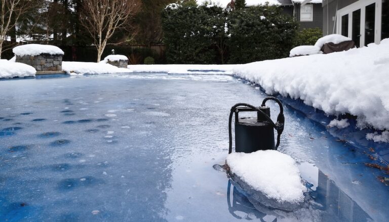 Automatic pool pump in ice and slush after snow storm. Inground backyard pool with black pool pump submerged in deep frozen water. Winterizing pool for cold or freezing temperature. Selective focus.